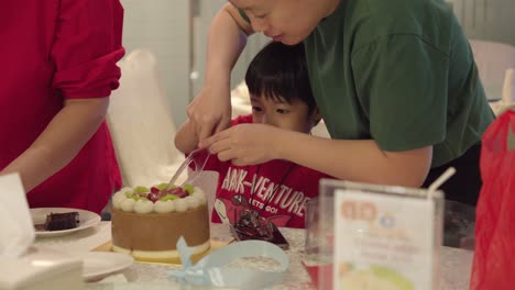 Un-Niño-Lleno-De-Alegría-Y-Emoción-Corta-Un-Pastel-De-Cumpleaños,-Guiado-Por-Un-Adulto.