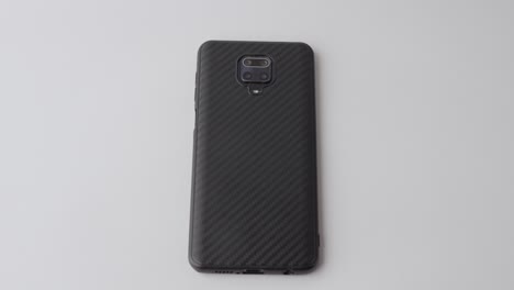 Hand-placing-a-carbon-fiber-textured-smartphone-on-a-white-surface