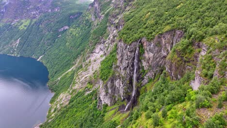 Vista-Aérea-De-La-Cascada-Sobre-El-Fiordo-De-Geiranger,-Magnífico-Paisaje-En-La-Temporada-De-Verano,-Noruega