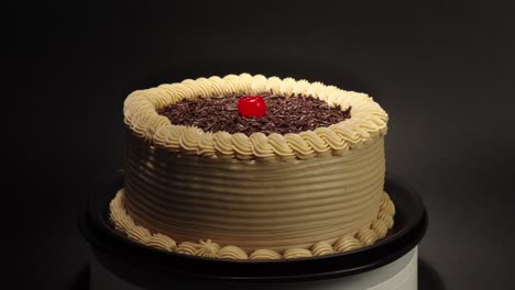 Mocha-cake-in-a-turn-table-with-black-background-mocca-moka-mochachino-with-shiny-cherry-on-top-fresh-delicious-tasty-dessert-party-celebratrion