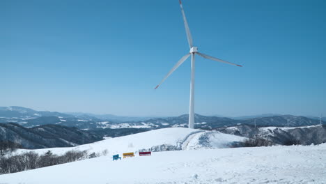 Una-Enorme-Turbina-Eólica-Gira-En-La-Cima-De-La-Montaña-En-Invierno-Contra-El-Cielo-Azul-En-El-Rancho-Daegwallyeong-Sky,-Daegwallyeong-myeon,-Pyeongchang-gun,-Gangwon-do,-Corea-Del-Sur.