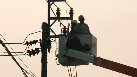 Hoisted-by-a-crane,-two-electric-repairmen-are-going-to-fix-some-of-the-electrical-problems-of-some-wires-in-a-neighborhood-in-Bangkok,-Thailand