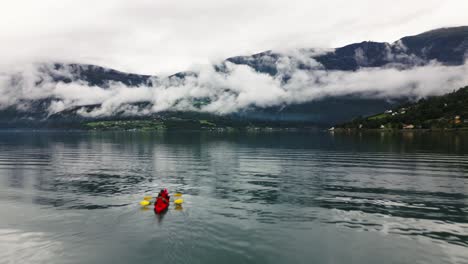 Paddelboot-Auf-Einem-Großen-Blauen-See-Mit-Hohen-Bergen-Und-Wolken-Im-Hintergrund,-Norwegen,-Natur,-Drohne