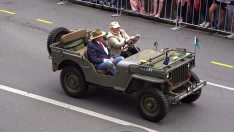 Veteran-riding-on-military-Willys-jeep-riding-down-the-street,-followed-by-Fifth-battalion-The-Royal-Australian-Regiment-Association-at-Anzac-Day-parade,-handheld-motion-close-up-shot