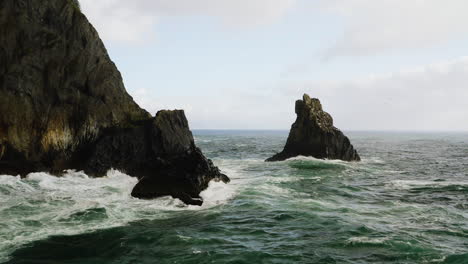 Low-flight-over-churning-waves-of-Pacific-Ocean-past-rock-covered-in-sea-birds