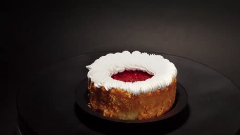 mini-cheesecake-petite-petit-personal-individual-portion-in-a-turn-table-with-black-background-loop-with-cream-on-top-and-berries-strawberry-jelly