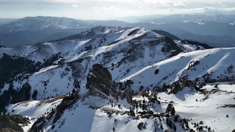 Snow-capped-Ciucas-Mountains-under-a-blue-sky,-with-rugged-terrain-casting-shadows-in-the-late-afternoon-light,-wide-shot