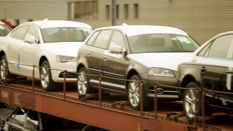 Nuevos-Coches-Audi-Transportados-En-Plataforma-De-Tren,-Entorno-Industrial,-Día-Nublado,-Movimiento-Borroso