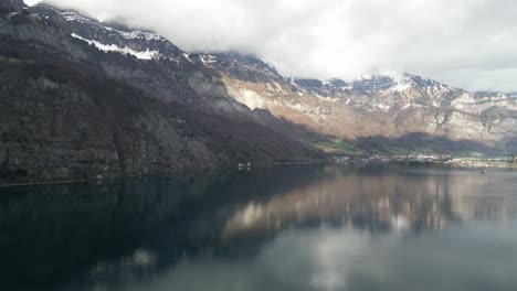 From-an-aerial-perspective,-the-rugged-beauty-of-mountain-landscapes-juxtaposed-with-a-quaint-residential-area,-all-against-the-stunning-backdrop-of-Walensee-Unterterzen,-Switzerland