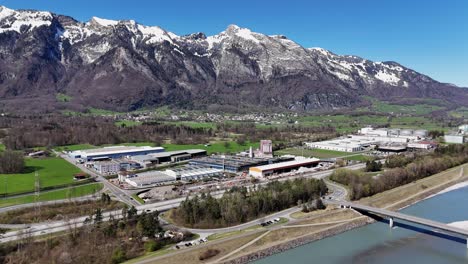 Sennwald-industrial-area-in-switzerland-with-mountains-in-the-backdrop,-sunny-day,-aerial-view