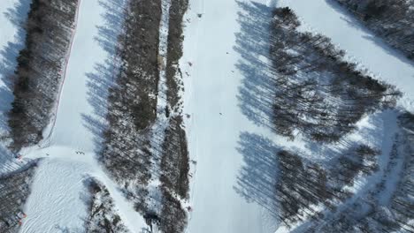 Top-down-tracking-shot-flying-down-mountain-following-ski-area,-high-angle-flying-forwards