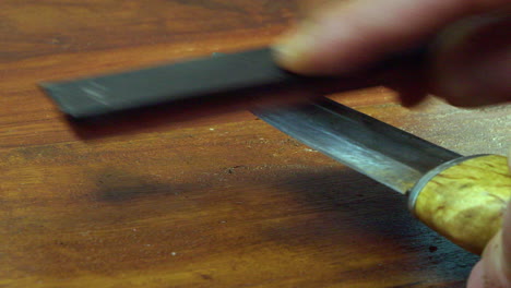 Man-hones-sharp-edge-of-forged-knife,-countertop-close-up-view