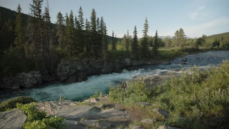 A-tranquil-mountain-river-courses-energetically-through-a-verdant-forest-as-the-evening-sun-bathes-the-landscape-in-soft-light