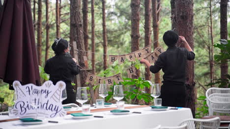 Gente-Preparando-Una-Pancarta-De-Fiesta-Para-Una-Alegre-Celebración-En-El-Jardín-Forestal