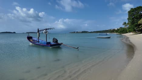 Tranquila-Playa-Tailandesa-Con-Barcos-En-Un-Día-Despejado,-Arenas-Doradas-Que-Se-Curvan-Hacia-Una-Exuberante-Vegetación-Y-Un-Sereno-Paisaje-Marino