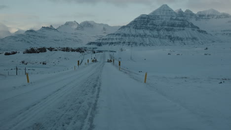 Establishing-view-of-Icelandic-asphalt-road-covered-in-snow-and-ice-at-sunset