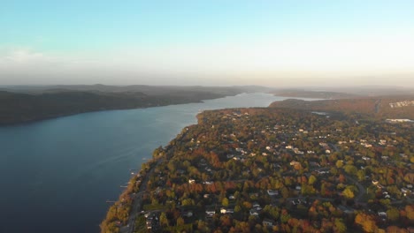 Aerial-shot-showcasing-a-long-river-flowing-between-to-large-pieces-of-land-during-golden-hour-with-autumn-colored-leaves