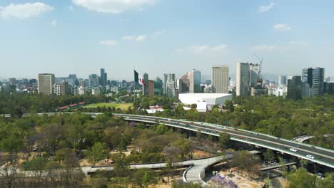 Aerial-view-moving-away-Chapultepec,-Mexican-flag,-Auditorio-Nacional,-avenues,-cars-and-Mexico-City