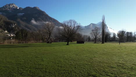 Low-angle-aerial-shot-of-a-mountain-with-a-green-field-in-foreground-in-Walensee,-Switzerland