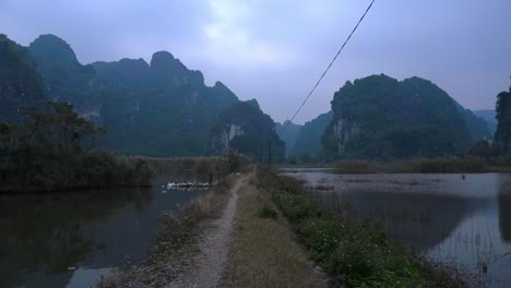Empty-Path-Between-Wetland-Waters-With-Silhouette-Of-Towering-Cliffs-In-Background-At-Ninh-Binh,-Vietnam