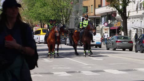 Mounted-police-patrolling-on-Sveavägen-in-Stockholm,-civilians-nearby,-sunny-day