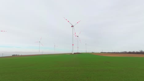 Grünes-Grasland-Mit-Windrädern-An-Land,-Die-Sich-Drehen,-Um-Strom-Zu-Erzeugen