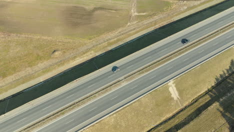 Two-cars-travel-on-an-open-highway,-casting-long-shadows-in-the-warm-light