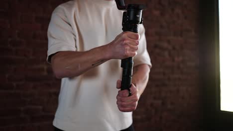 Male-at-indoor-studio-with-bright-sunlight-from-window-hold-gimbal-stabilizer