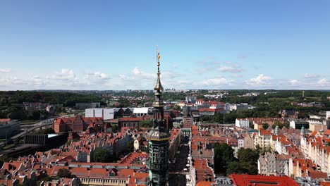 gold-spire-of-an-big-tower,-beautiful-old-town-city-centre-with-many-red-houses-in-gdansk,-danzig,-gdansk,-poland,-europe,-drone