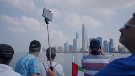 Abu-Dhabi,-Emiratos-Árabes-Unidos,-Turistas-Tomando-Selfies-Y-Fotografías-Del-Paisaje-Urbano-Desde-Un-Barco-De-Crucero-En-El-Mar