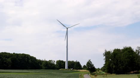 Una-Turbina-Eólica-Es-Alta-Y-Blanca,-De-Pie-En-Un-Campo