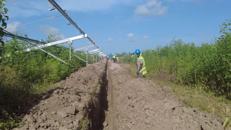 POV-walking-through-trench-while-african-workers-dig-with-shovels-at-construction-site-in-Jambur,-Gambia