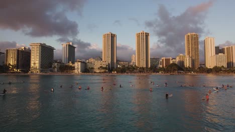 People-Surfing-At-Waikiki-Beach-Coastline-at-Sunset,-Aerial-Drone-Flyover