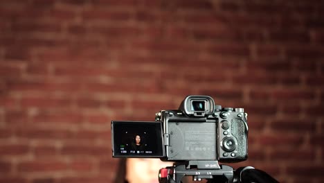 Digital-camera-on-tripod-at-indoor-studio-record-female-near-red-brick-wall