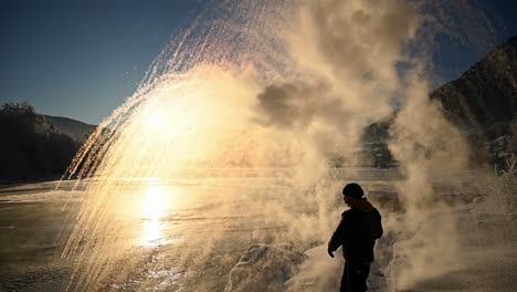 Person-Wirft-Kochendes-Wasser-In-Die-Luft,-Das-Sich-Vor-Einem-Wintersonnenuntergang-In-Schnee-Verwandelt,-Zeitlupen-Handkamera