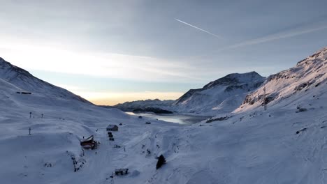 Morgendämmerung-Auf-Wunderschönen-Schneebedeckten-Bergen-Mit-Zugefrorenem-See-Und-Schutzhaus,-Mont-Cenis