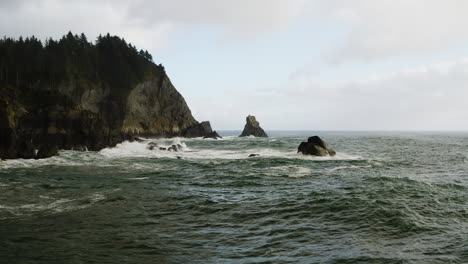 Vuelo-Bajo-Sobre-Las-Agitadas-Olas-Del-Océano-Pacífico-En-La-Costa-De-Oregon,-Hacia-Una-Pequeña-Pila-De-Mar