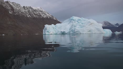 Iceberg-En-Agua-De-Mar-Fría-Bajo-Colinas-Cubiertas-De-Nieve-En-El-Fiordo-Noruego