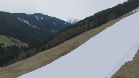 Los-Esquiadores-Descienden-Por-Una-Pendiente-Parcialmente-Cubierta-De-Nieve-En-Saalbach-hinterglemm,-Contraste-De-Estaciones