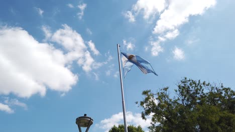 Bandera-Argentina-Ondeando-En-El-Brillante-Horizonte-De-La-Plaza-Pública-Urbana-De-Buenos-Aires,-Símbolo-Nacional-De-La-Independencia,-Blanco-Y-Azul-Claro-Con-Sol