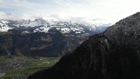 Aerial-viewpoint,-the-valley-of-Glarus,-Switzerland,-is-showcased,-featuring-residential-communities-nestled-amidst-the-majestic-snow-capped-peaks-of-the-Swiss-Alps