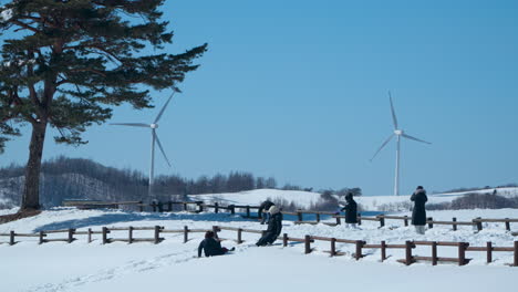 Familia-Disfrutando-Del-Día-En-La-Nieve,-Cerca-De-Turbinas-Eólicas,-Daegwallyeong-Sky-Ranch,-Corea