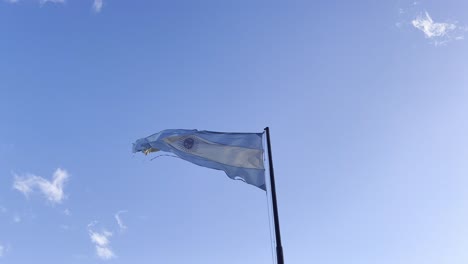 Torn-flag-of-Argentina-waving-in-the-wind-against-blue-skies,-60fps