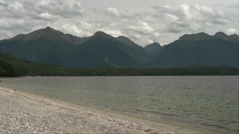 The-tranquil-lake-nestled-in-Fiordland,-New-Zealand,-with-lush-mountain-trees-in-the-backdrop,-forms-a-striking-panorama