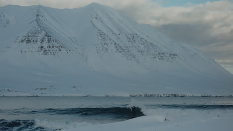 Tracking-pan-follows-surfer-cutting-back-and-carving-along-face-of-wave-in-arctic-snow-conditions
