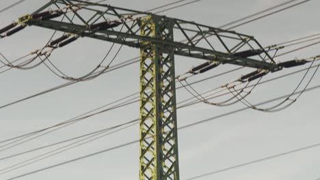 Close-up-of-a-green-electricity-pylon-with-cables-against-cloudy-sky,-tilt-up-shot