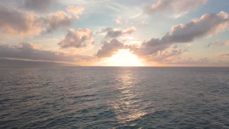 Flying-above-wavy-Pacific-ocean-toward-bright-sunset-near-horizon,-Hawaii