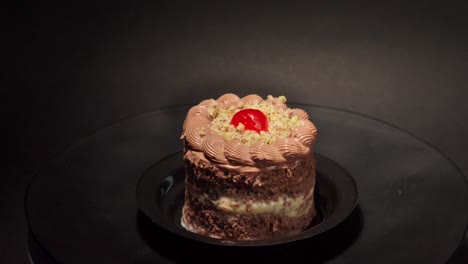 mini-petite-individual-portion-slice-of-Chocolate-and-cheese-cake-in-a-turn-table-with-black-background-with-cherry-on-top-and-nuts-tasty-yummy-delicious