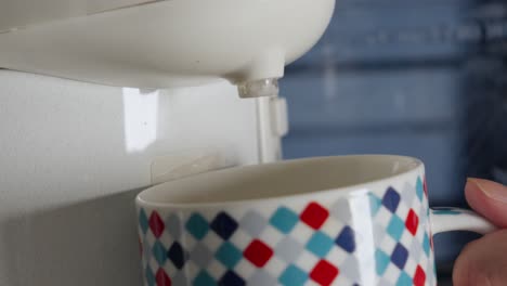 Water-Poured-From-White-Plastic-Water-Dispenser-Tap-Into-Checkered-Pattern-Mug,-Close-Up