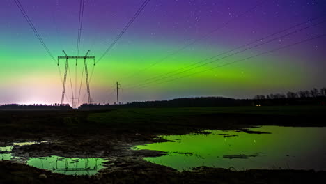 Beautiful-time-lapse-of-the-northern-lights-in-the-night-sky-that-are-reflected-in-puddles-of-water,-with-electric-antennas-in-the-background